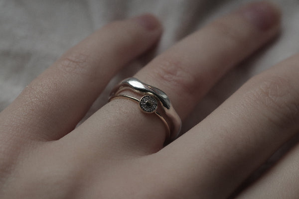 Close-up of a hand wearing a silver ring with a small gemstone on a neutral background